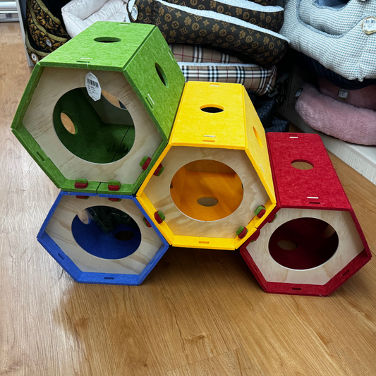 Colorful hexagonal pet toys stacked on a wooden floor with pet beds in the background.